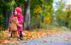 Маленькая девочка с медвежонком на дороге осенью 