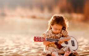 Маленькая девочка с гитарой сидит на песке 