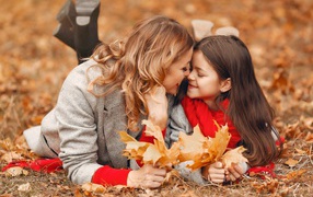 Мама с дочкой лежат на листве осенью 