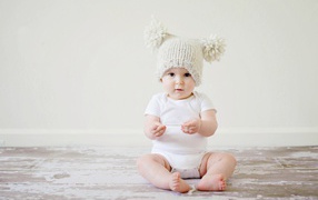 Маленький грудной ребенок в боди с шапкой на голове