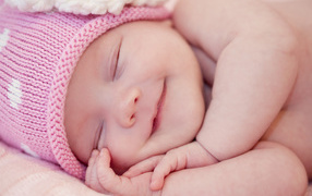 Улыбающийся грудной ребенок в розовой вязаной шапке 