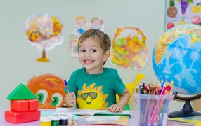 Улыбающийся мальчик школьник с канцелярскими предметами на столе 