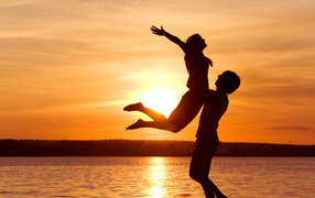 The guy raises the girl in his arms at sunset