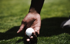 Белый мячик для гольфа в руке у мужчины на поле 