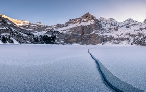 Трещина в озере на фоне заснеженных гор зимой