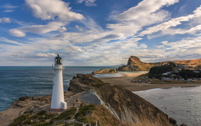 Lighthouse on a rocky shore under a blue sky with white clouds by the sea, New Zealand