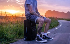 Мужчина с татуировками на теле сидит на чемодане 
