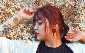 Молодая девушка с татуировкой на руке стоит у цветущего дерева