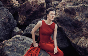 Актриса Милла Йовович в красном платье сидит на камне