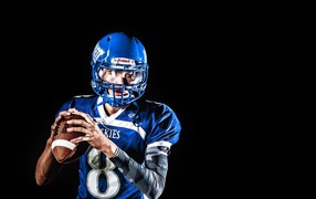 Игрок в американский футбол с мячом в руках на черном фоне 
