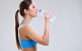 Красивая спортивная девушка пьет воду на сером фоне 