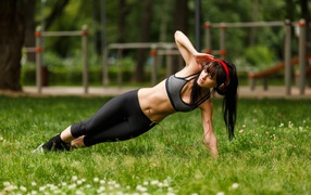 Девушка с наушниками на голове занимается фитнесом на траве 