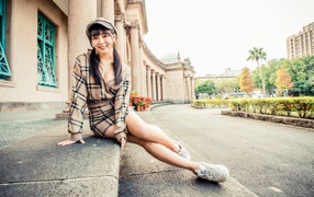 Улыбающаяся азиатка в кепке сидит на ступеньках 