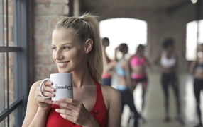 Улыбающаяся спортивная девушка с чашкой кофе у окна