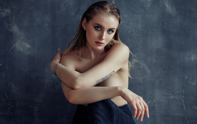 Нежная девушка с татуировками на теле сидит у стены