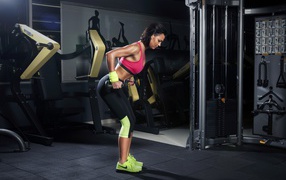 Девушка занимается с гантелями в спортзале у тренажеров 