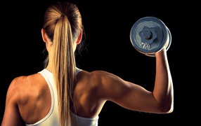 Young girl shakes hand dumbbell on a black background