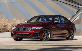 BMW M550i XDrive burgundy sedan, 2021 in front of the building