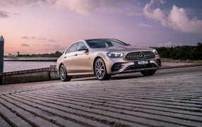 Серебристый автомобиль Mercedes-Benz E 300 E AMG Line 2021 года у реки