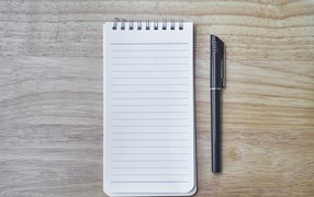 Авторучка и блокнот лежат на деревянном столе