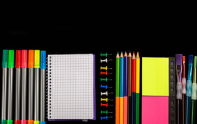 Фломастеры, карандаши, тетрадь и кисточки на черном фоне 