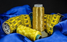 Золотые нитки и сантиметр на голубой ткани 