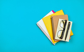 Блокноты, очки и ручка на голубом фоне