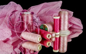 Розовые нитки с сантиметром и тканью на черном фоне 