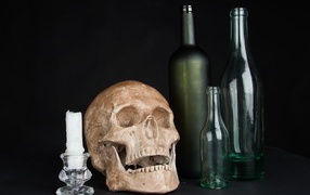 Череп, пустые бутылки и свеча на черном фоне