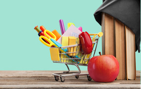 Канцелярские предметы в тележке на столе с яблоком и книгами 