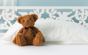 Игрушечный медвежонок сидит на белой постели