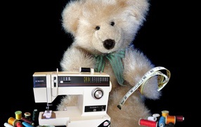 Игрушечный медвежонок со швейной машинкой на черном фоне 