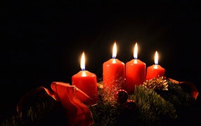 Три зажженные красные свечи с еловой веткой на черном фоне 