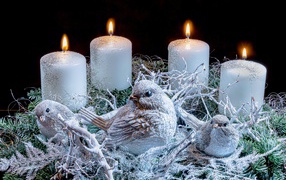 Три зажженные свечи со статуэтками птицами 
