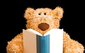Игрушечный медведь в очках с книгой на черном фоне