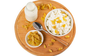Cottage cheese with raisins and milk on a board on a white background