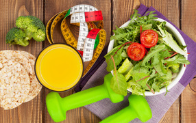 Салат из зелени на столе с соком и гантелями