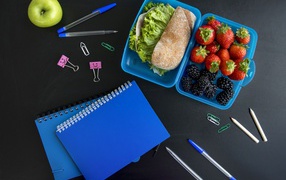 Сэндвич и ягоды в контейнере на столе с канцелярскими предметами