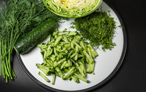 Sliced cucumbers with dill and cabbage on a black background
