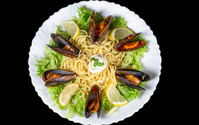 Спагетти с мидиями и листьями салата на белой тарелке