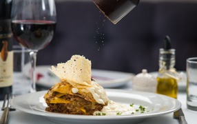 Кусок лазаньи посыпают перцем 