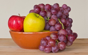 Яблоки и розовый виноград в тарелке на столе 