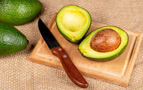 Зеленое авокадо с ножом на разделочной доске