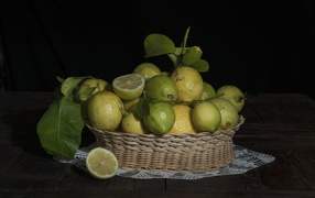 Лимоны и лаймы в плетеной корзинке на черном фоне