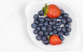 Много синей черники с клубникой в белой тарелке 