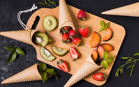 Вафельные рожки с ягодами и фруктами на доске 