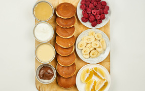 Pancakes with bananas, raspberries and orange on the table with sauces