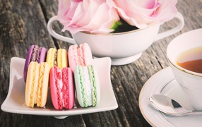 Десерт макарон на столе с чаем и цветами розы