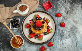 Оладьи с ягодами клубники и винограда на столе с медом