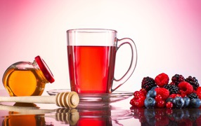 Чашка чая с медом на столе с ягодами